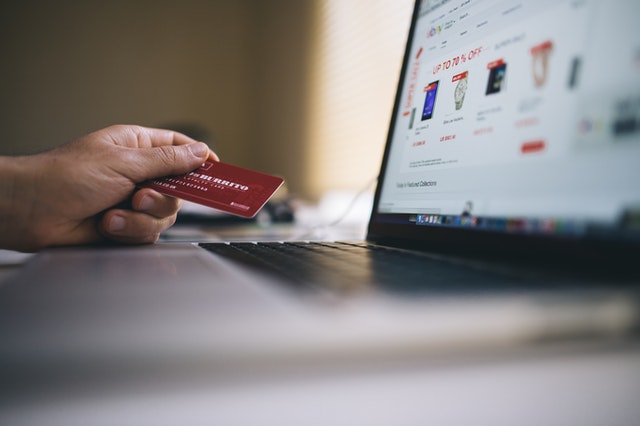 A person holds a credit card while looking at their laptop