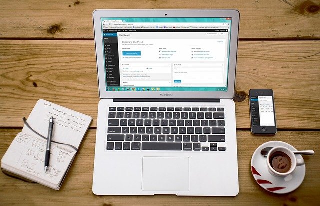 A laptop next to a notebook, smartphone, and cup of tea